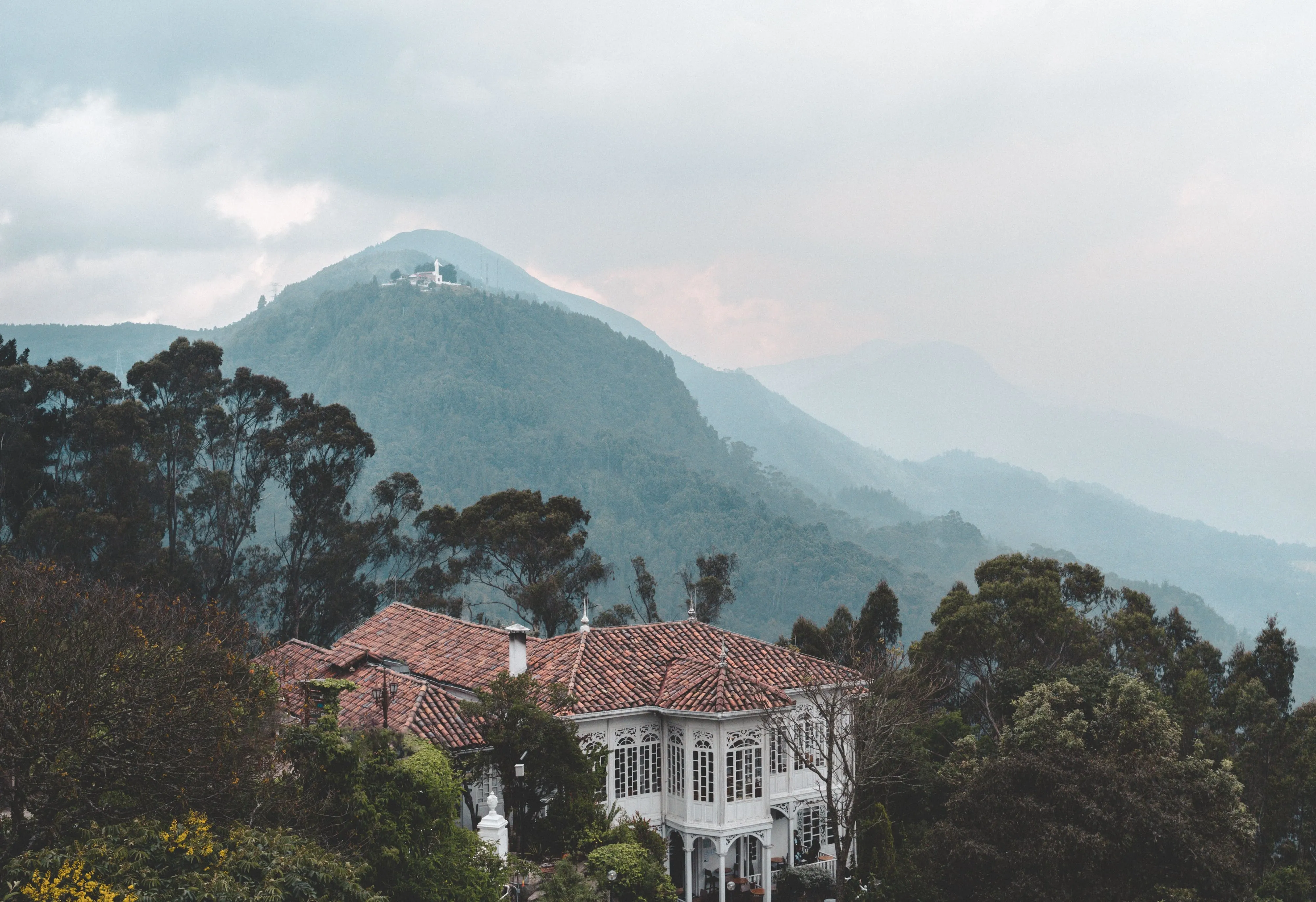 A white country house with a tiled roof beneath misty Andean hills
