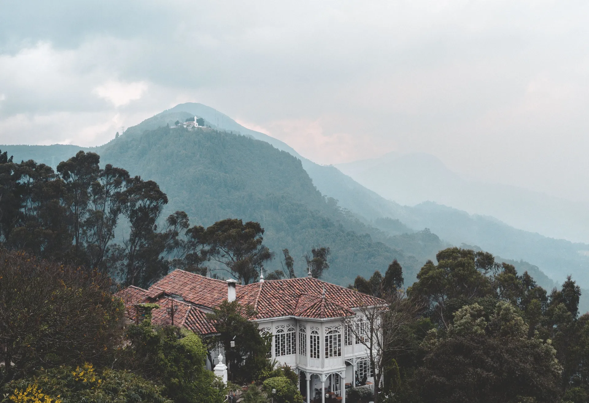 A small house on a misty green Andean hillside, low cloud sitting across the ridge behind it