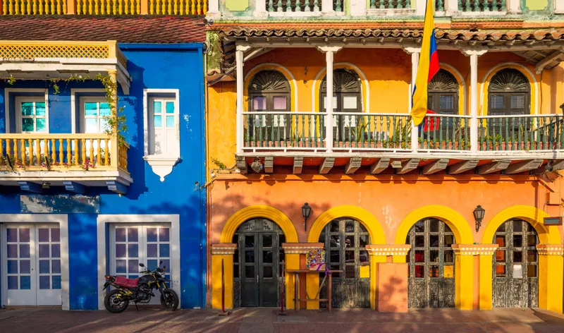 A narrow colonial street in Cartagena lined with brightly painted balconied houses and hanging flowers