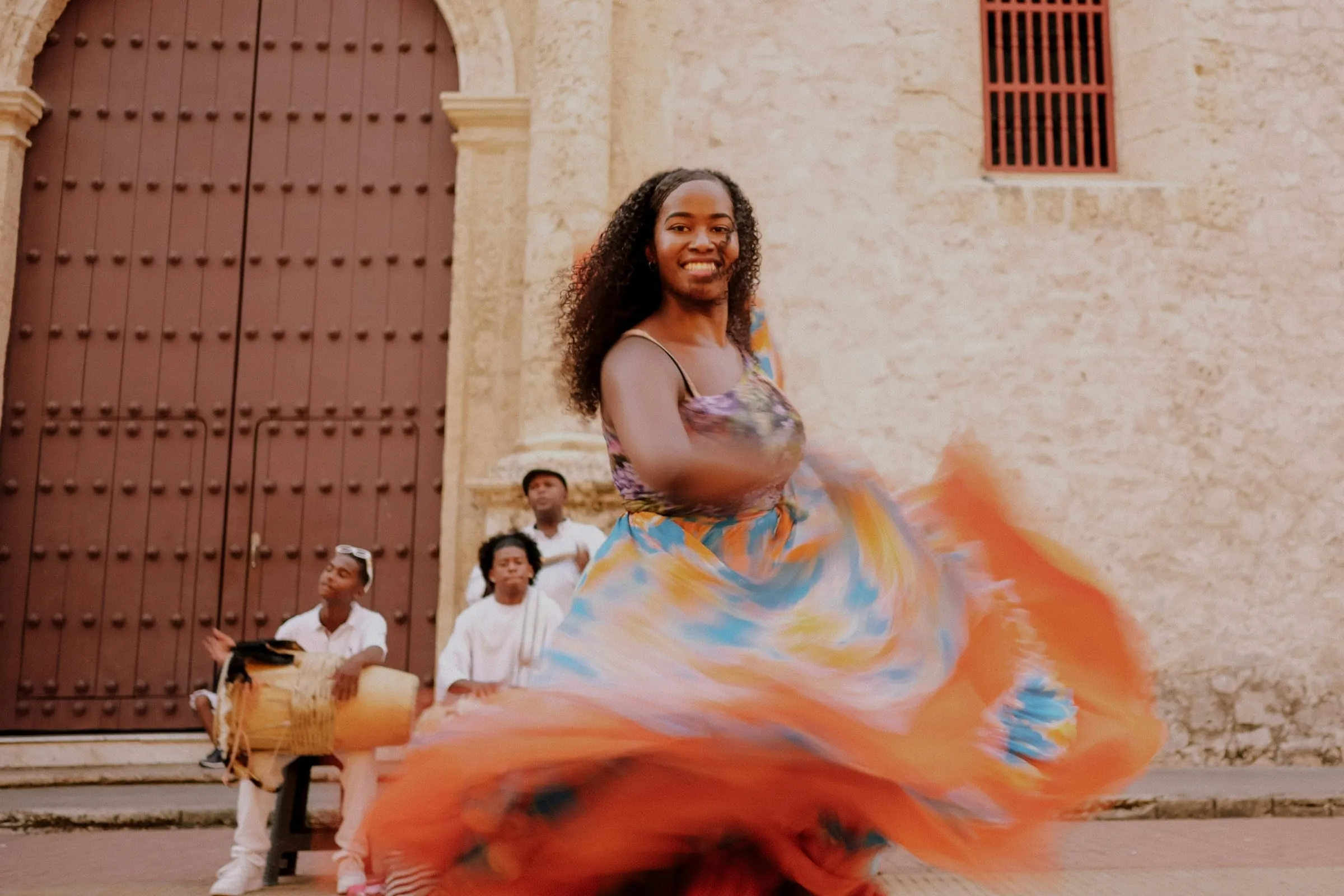A Colombian folk dancer spinning in a colourful skirt as drummers play outside a colonial church