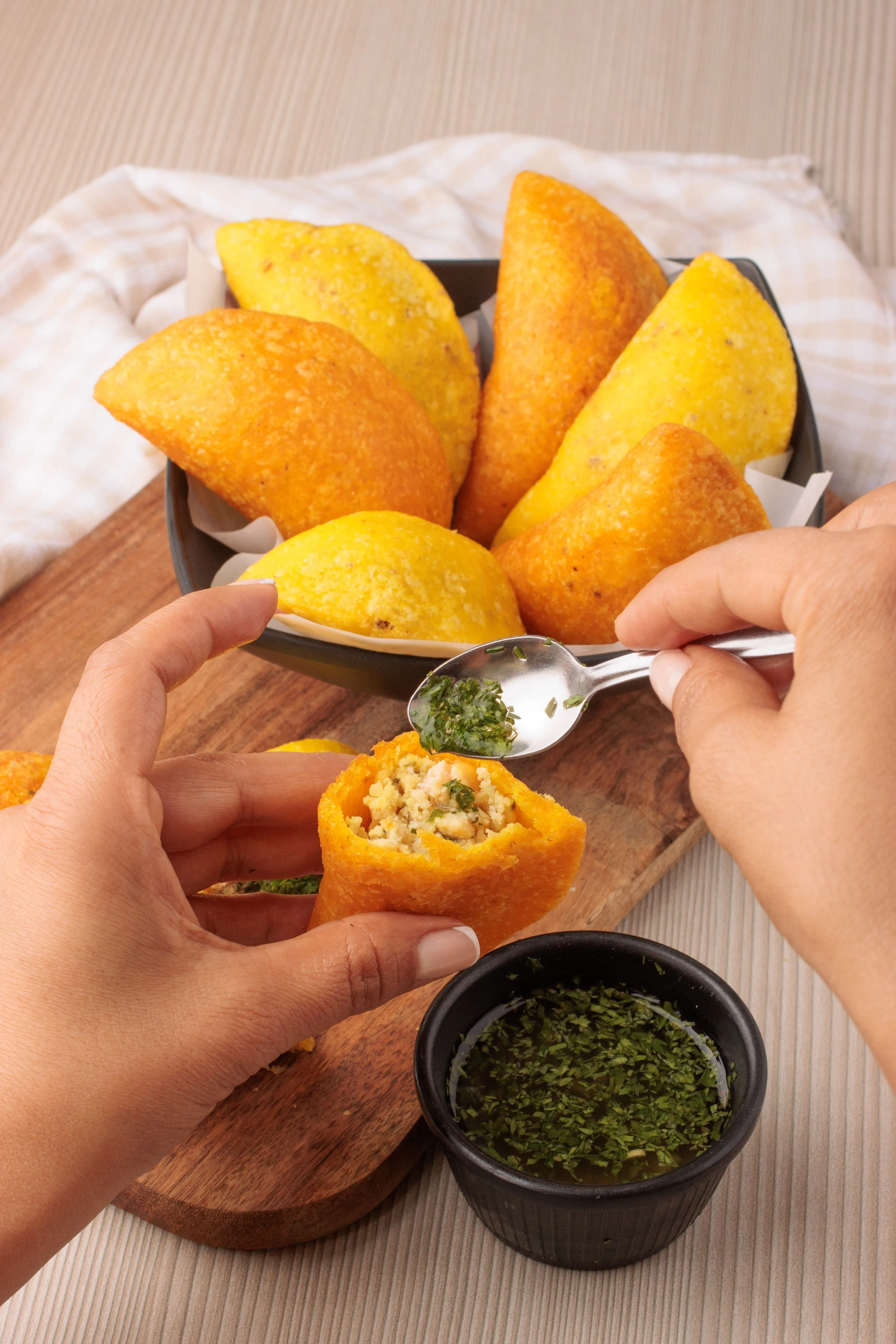 Golden corn-dough empanadas in a bowl, one broken open beside a dish of green ají sauce
