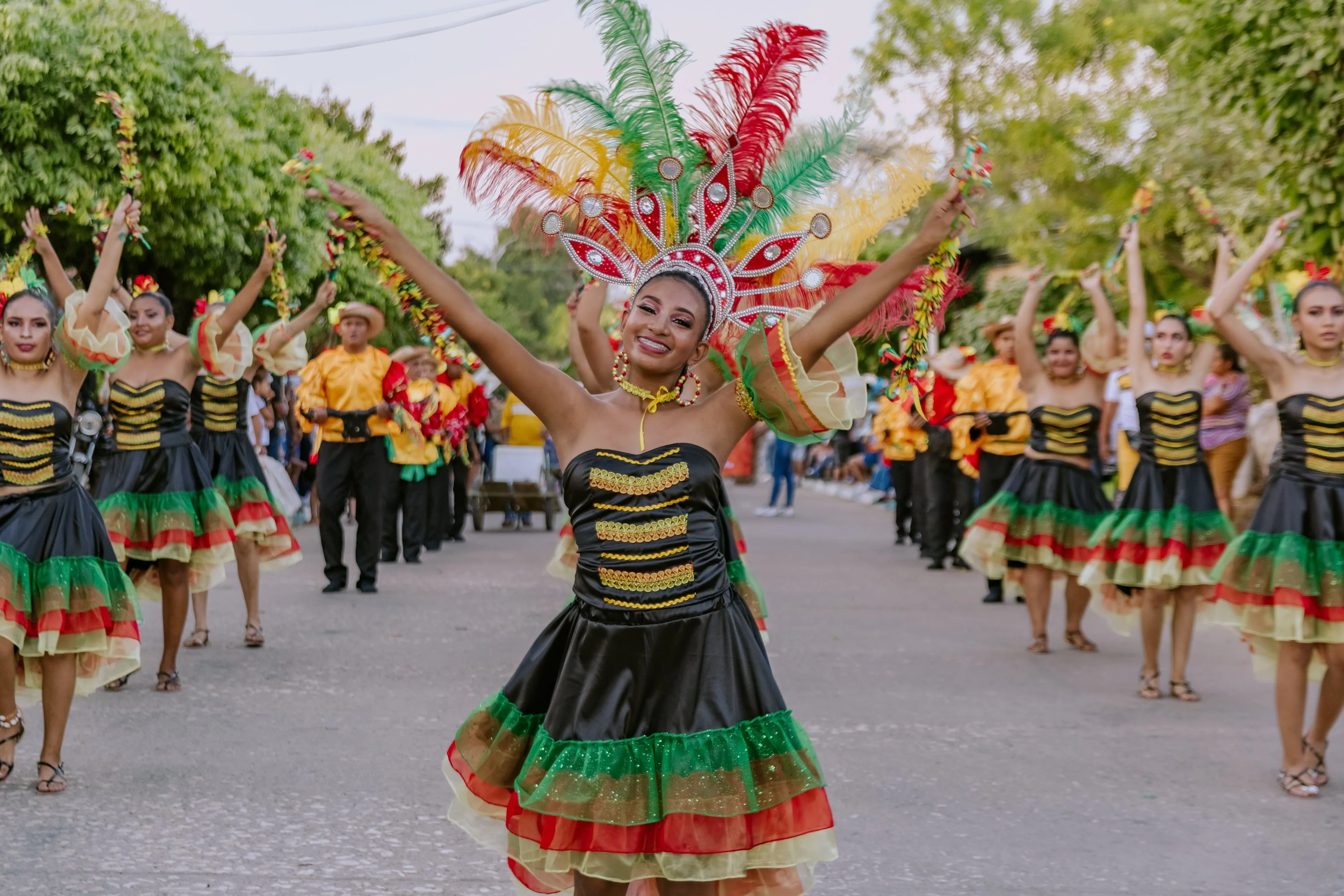 Parade dancers in ruffled costumes and tall feathered headdresses filling a street