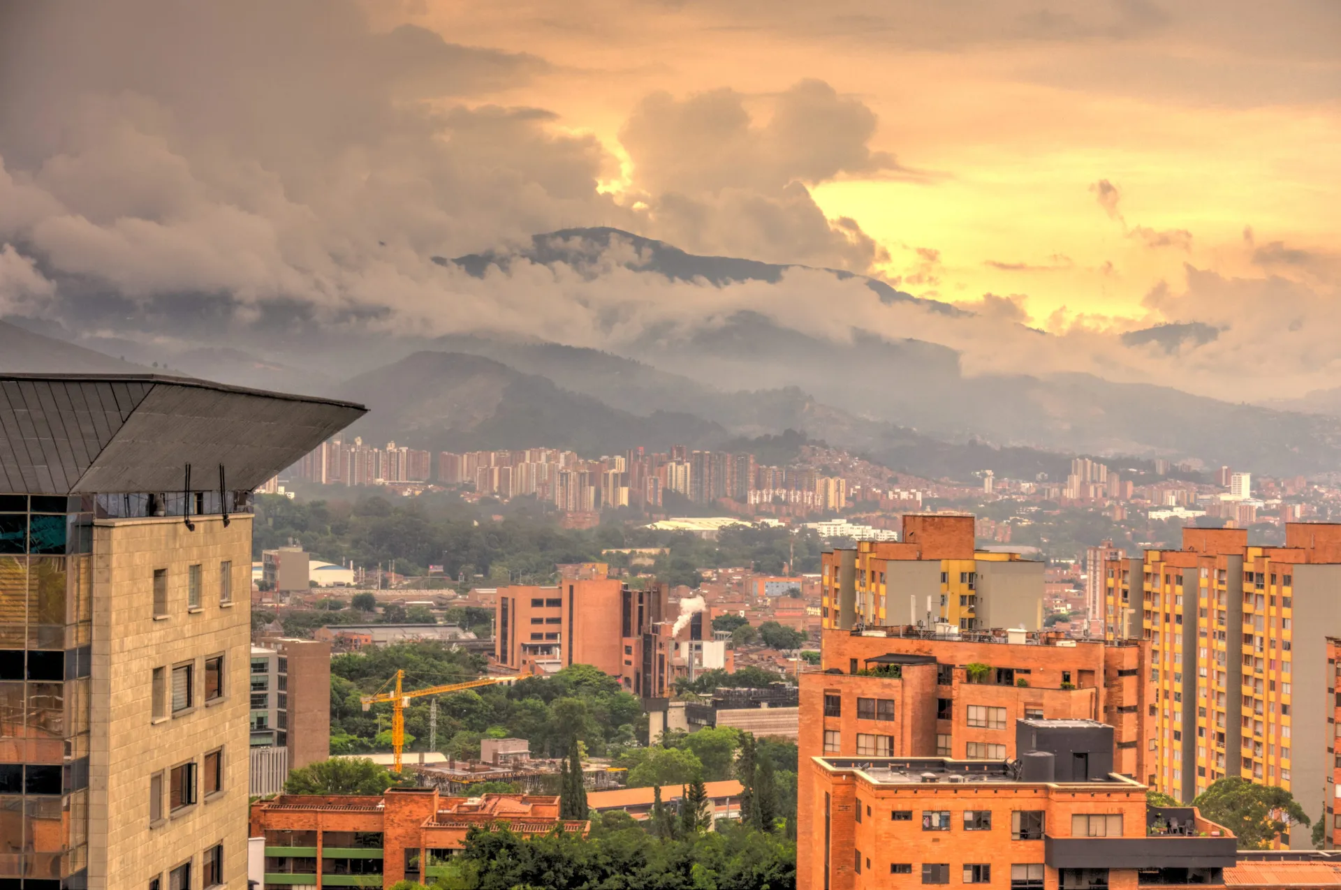 Red-brick apartment towers filling Medellín's Aburrá Valley at sunset, with cloud spilling over the mountains behind