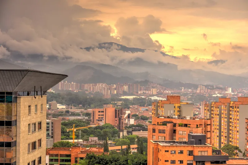 Red-brick apartment towers filling Medellín's Aburrá Valley at sunset, with cloud spilling over the mountains behind