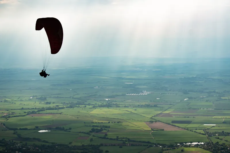 A paraglider silhouetted against the sky over the green valley near Medellín