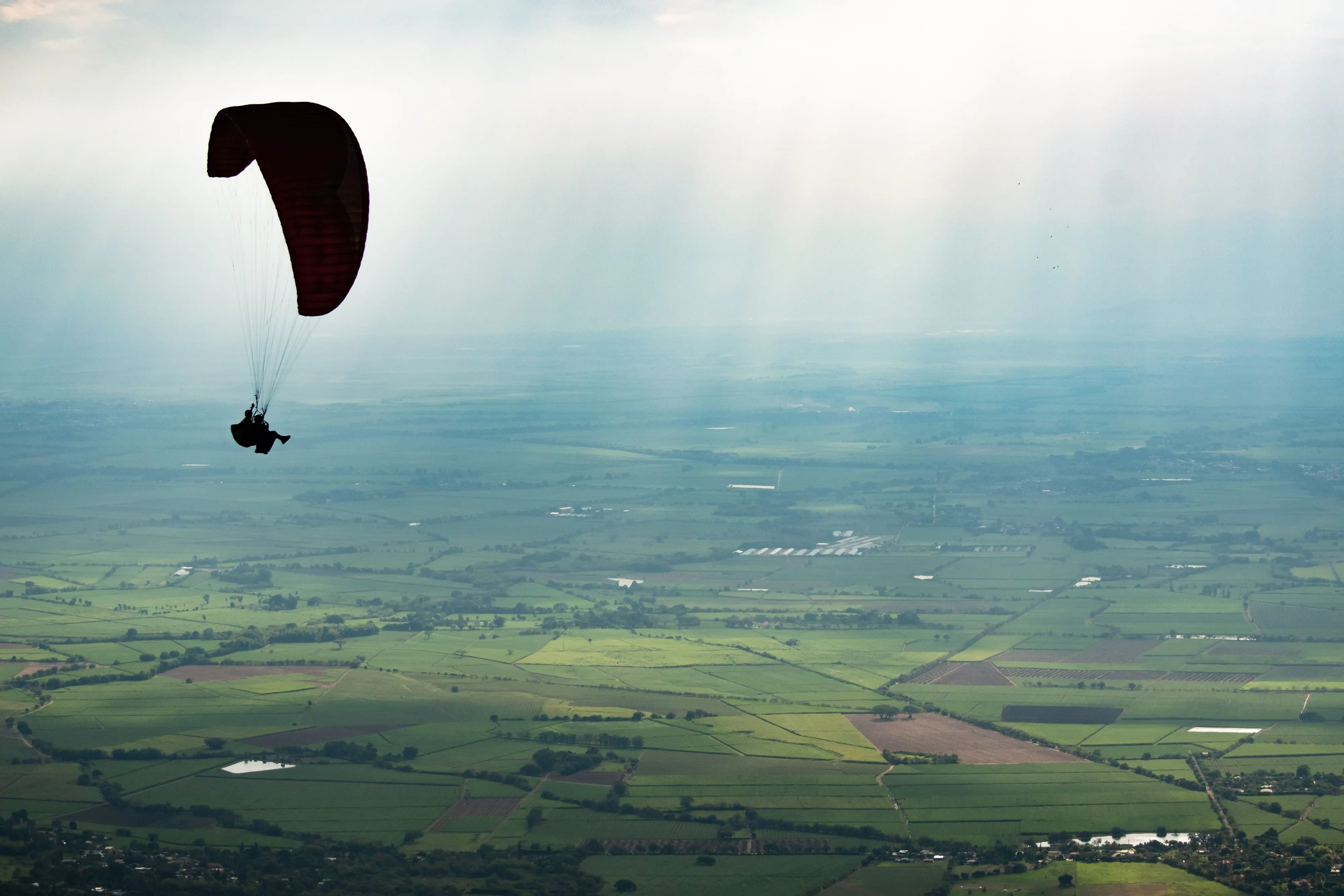 A paraglider silhouetted against the sky over the green valley near Medellín