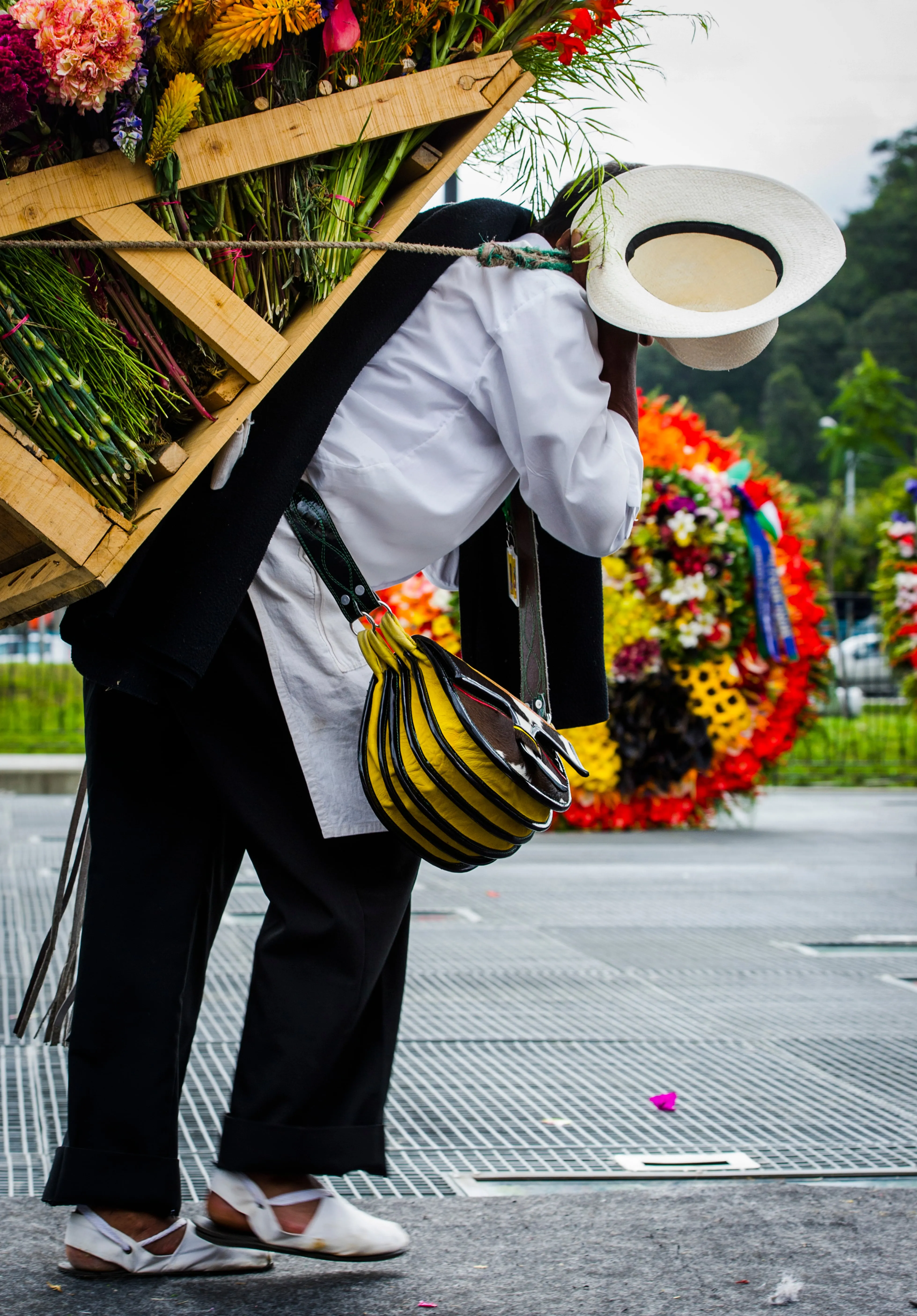 A silletero in a white shirt and poncho bent under the weight of a wooden frame stacked with flowers