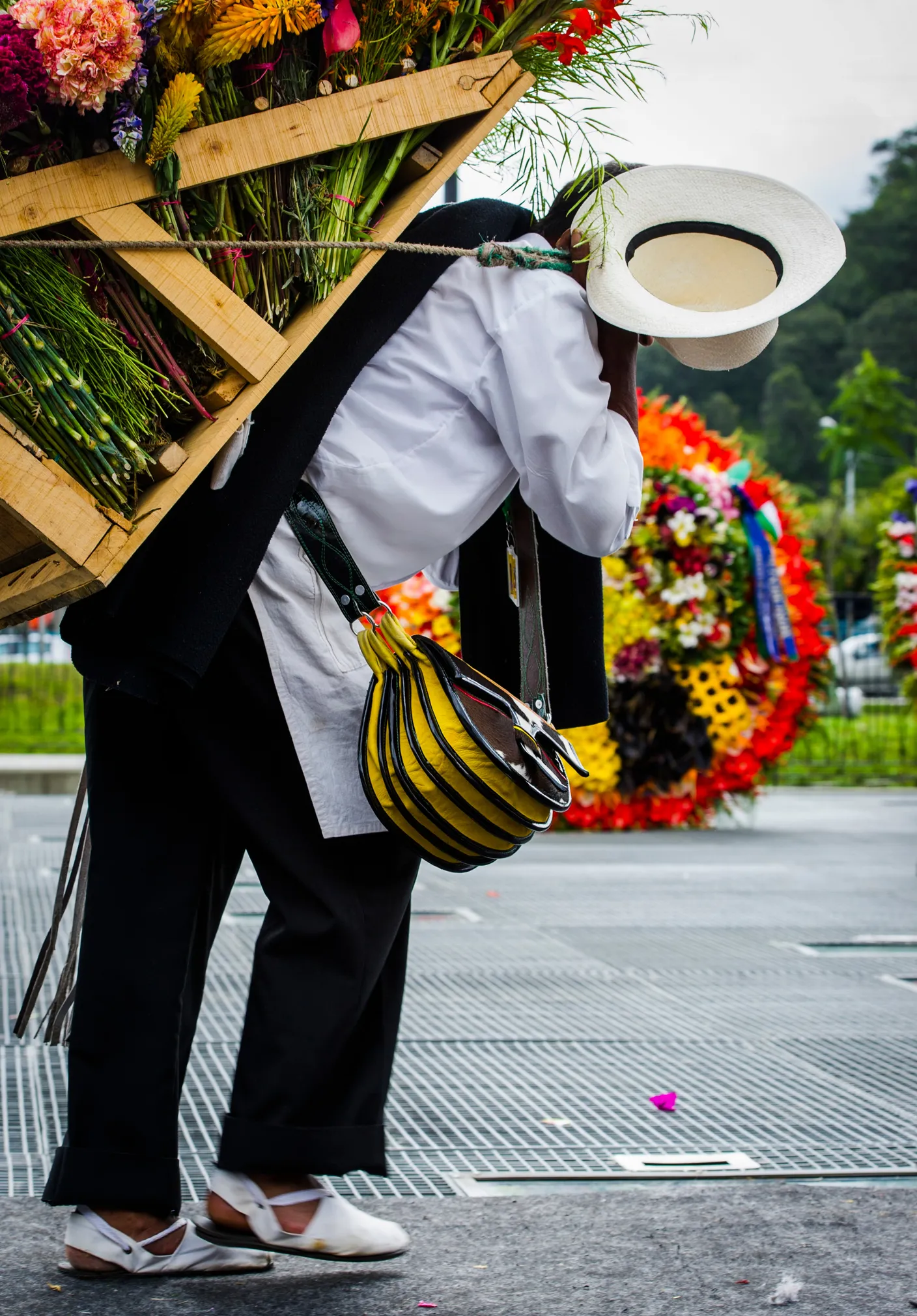 A silletero in a white shirt and poncho bent under the weight of a wooden frame stacked with flowers