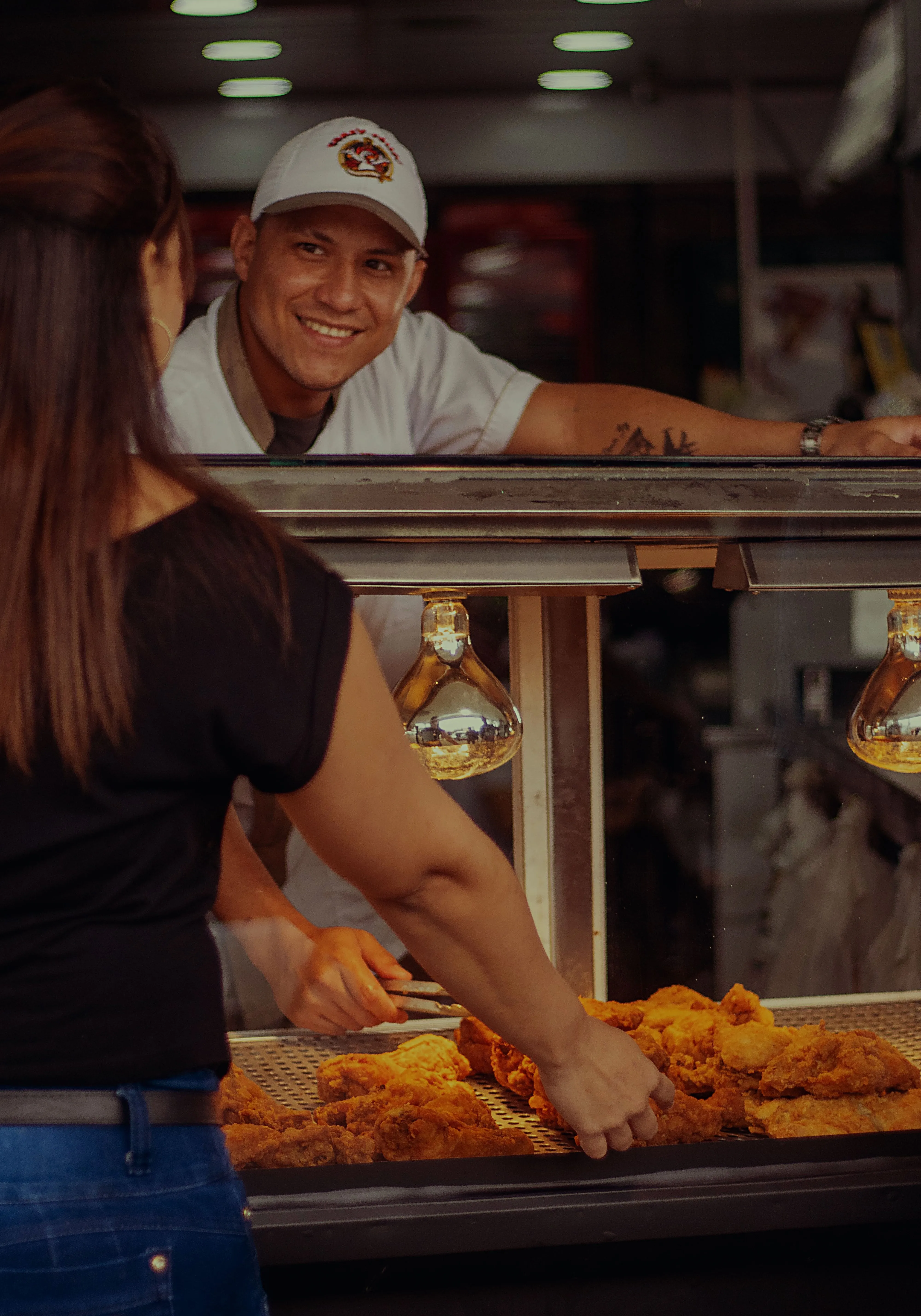A street food vendor at a lit counter handing over fried snacks to a customer