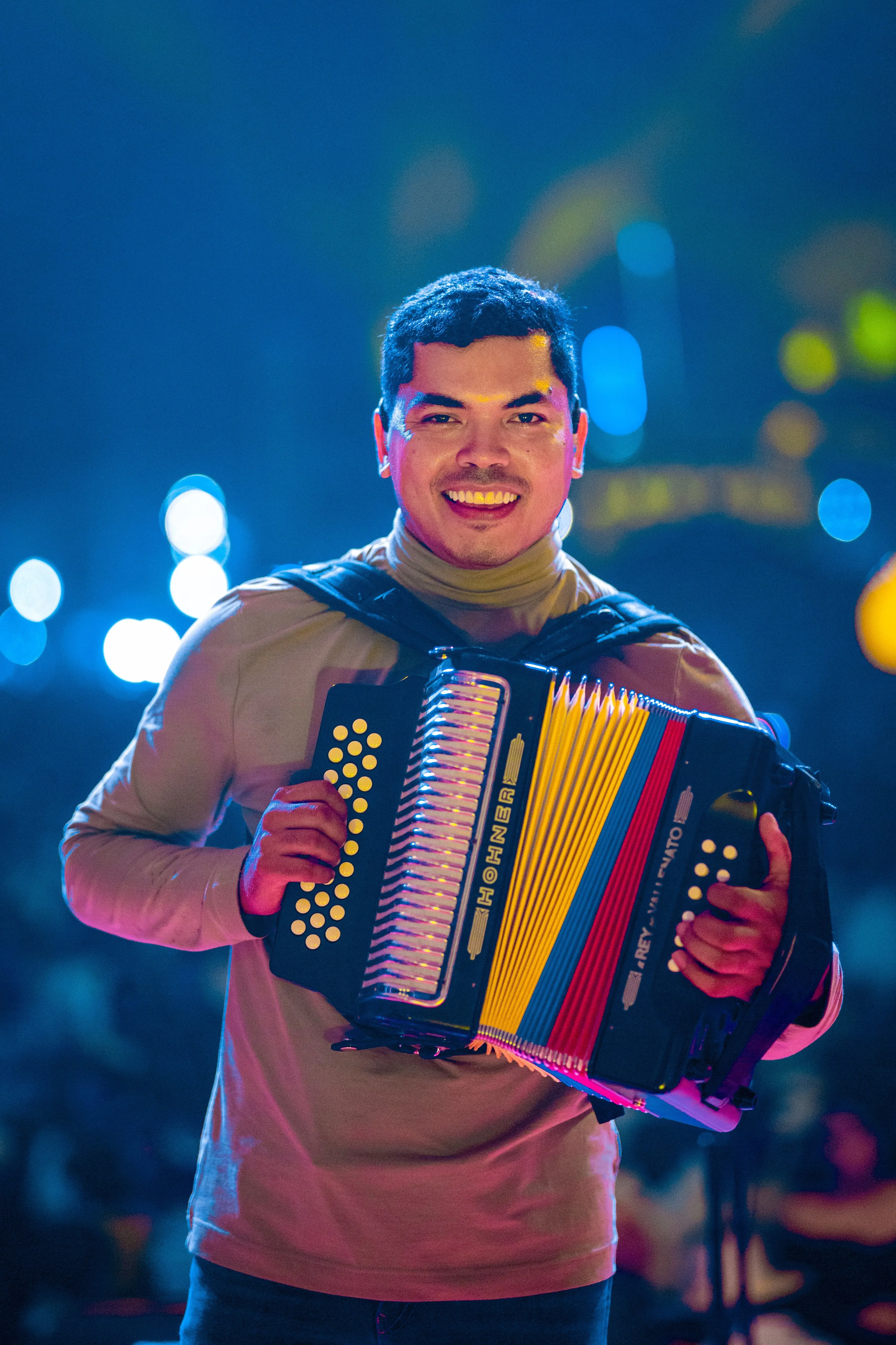 An accordionist on stage smiling behind a diatonic accordion with yellow, blue, and red bellows