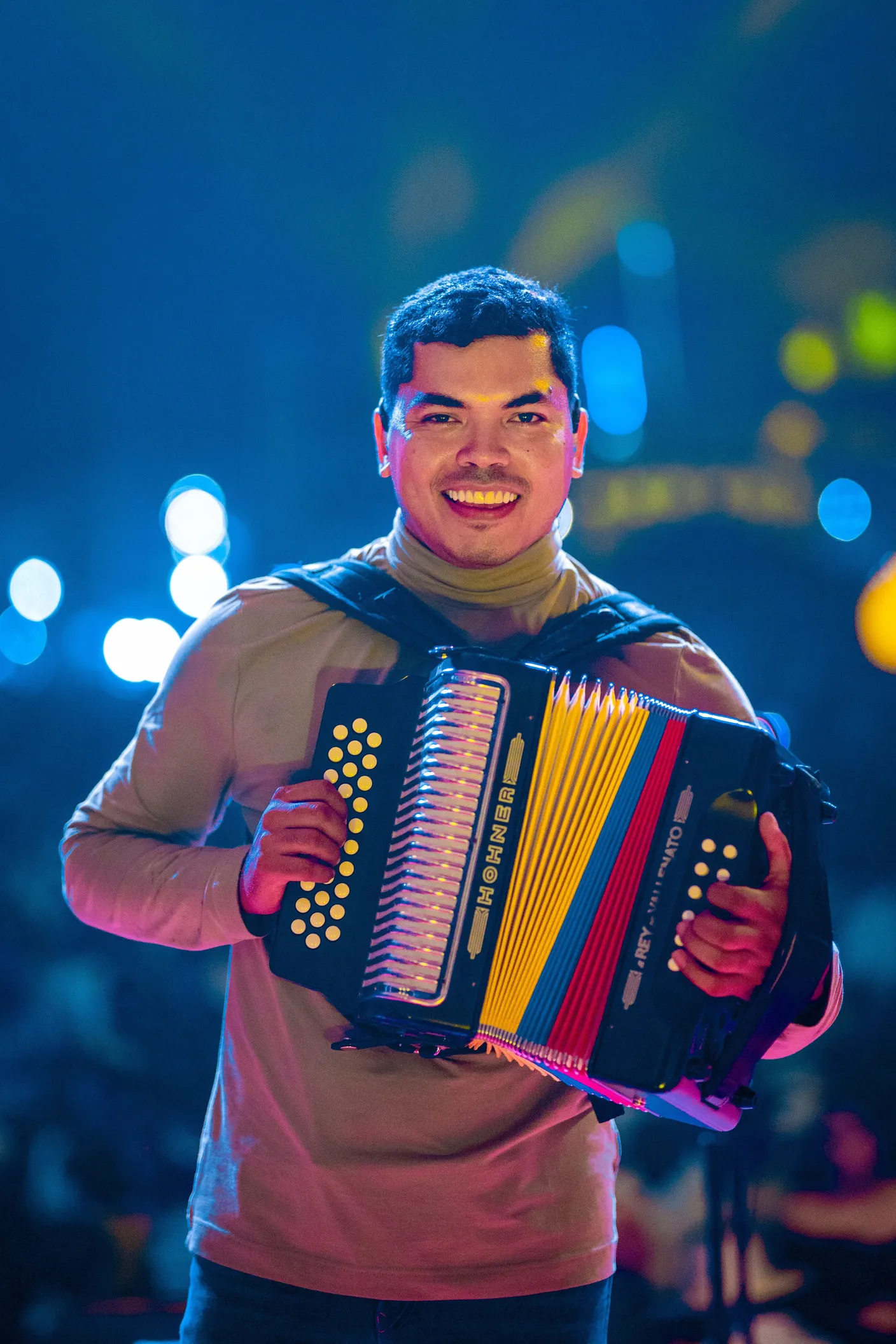 An accordionist on stage smiling behind a diatonic accordion with yellow, blue, and red bellows