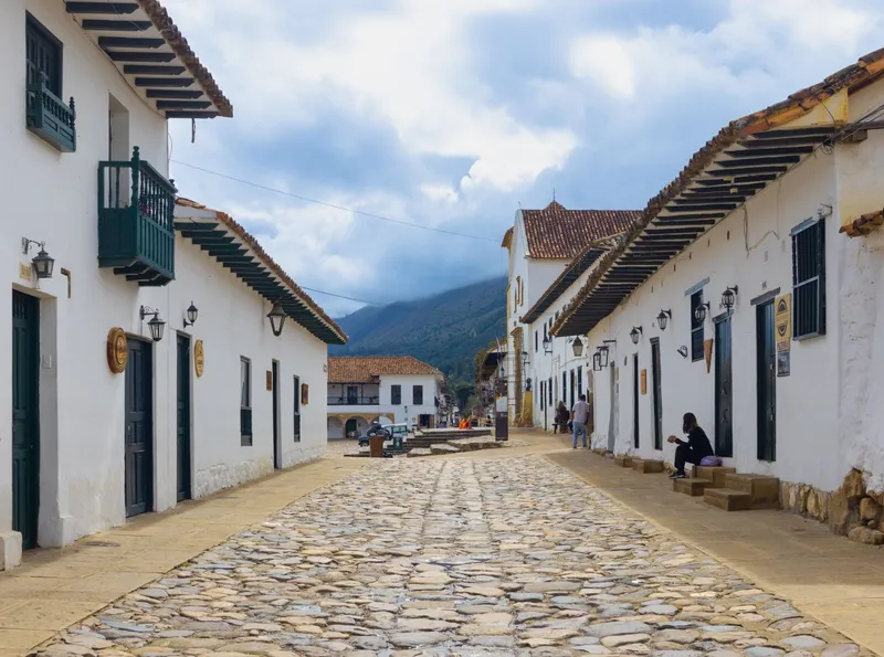 A cobbled street of whitewashed houses with green wooden balconies in Villa de Leyva, dry hills rising at the end of it